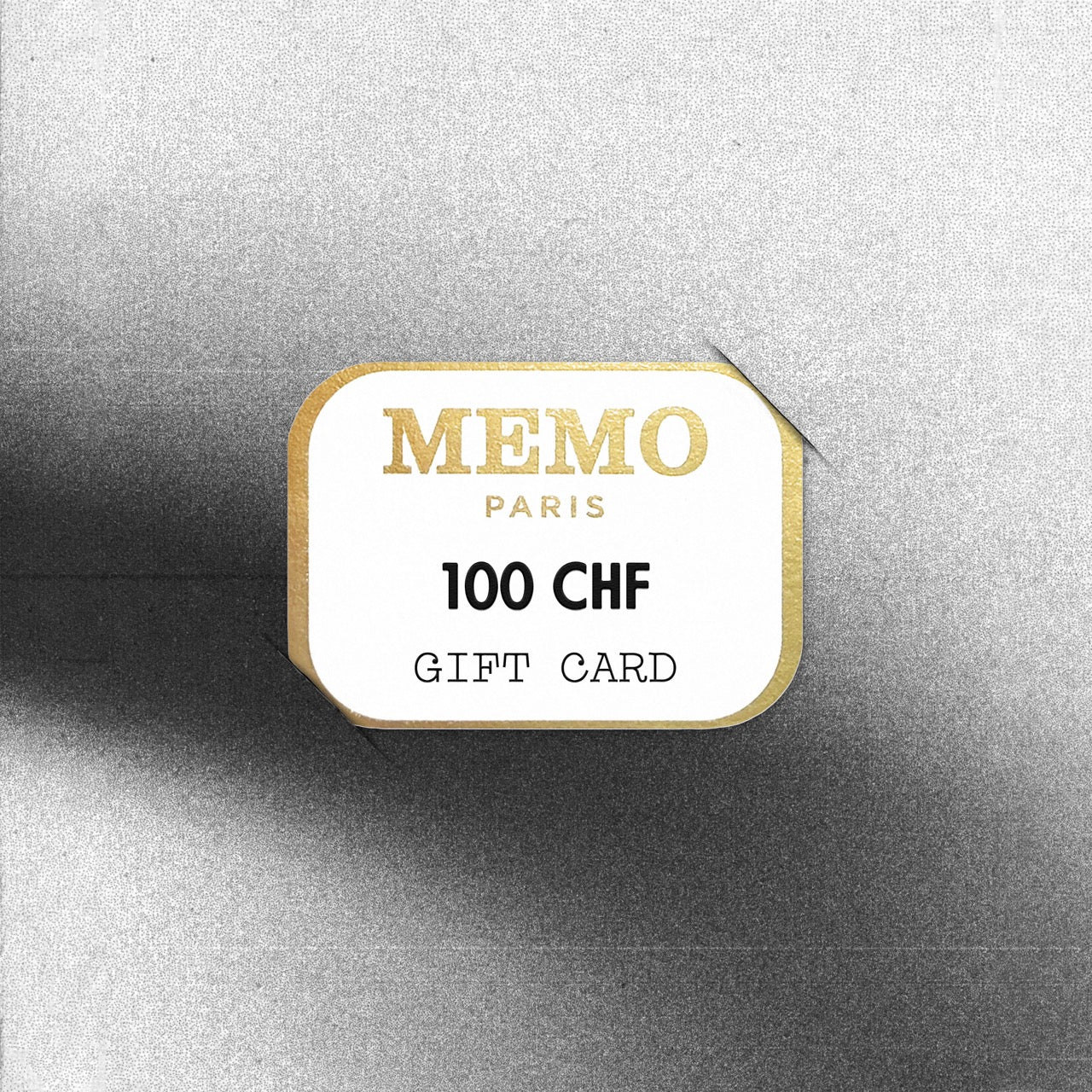 A white rectangular gift card with gold foil lettering and border from memo paris celebrating dream destinations worth 100 chf
