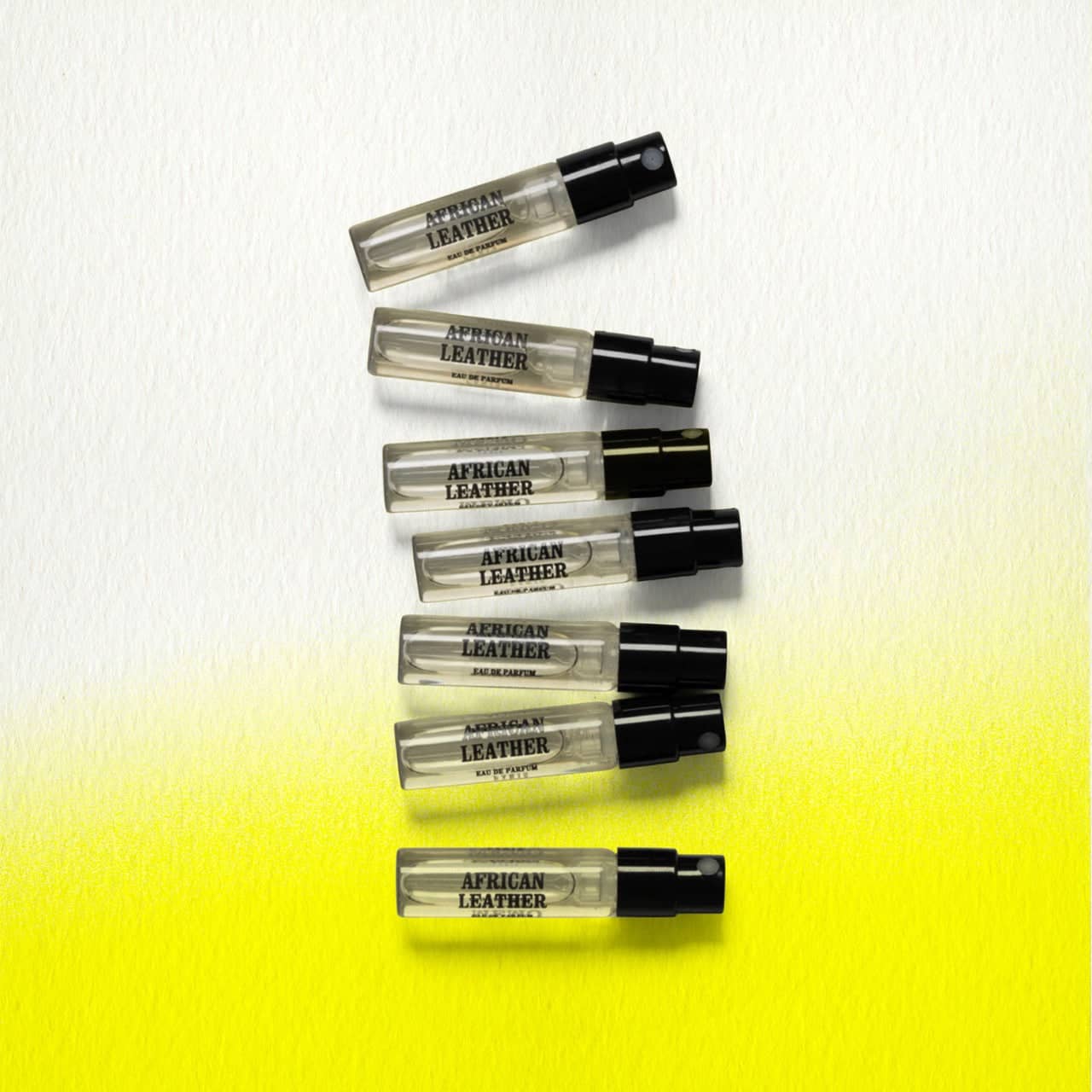 Six transparent glass vials of african leather eau de parfum, each with a black spray nozzle and minimalist label.